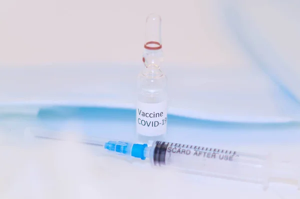 Bir şişe Coronavirus aşısı, beyaz stüdyo ve maske arka planında enjeksiyon şırıngasıyla birlikte..