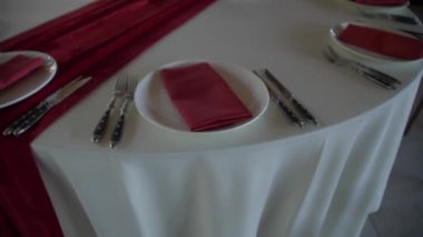 Ziyafet masası. Kırmızı peçetelerle beyaz bir masa örtüsü üzerinde servis yapmak. Beyaz tabak ve çatal bıçak takımı.