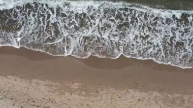 Açık havada kumlu bir sahilde süzülen deniz dalgalarının hava görüntüsü. İHA 4K. Kuş bakışı.