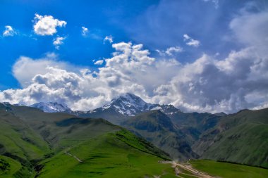 Mavi gökyüzü ve bulutların arkasındaki Kazbek dağı