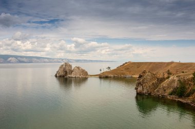 Şamanka Kayası ve Sibirya 'nın doğusundaki Baykal Gölü' nün Olkhon Adası 'nın ana köyü Khuzhir yakınlarında bulutlu bir günde kıyıların dağlık kesimi. Fotoğrafta küçük bir turist gemisi görebilirsiniz. Fotoğraf Temmuz 'da yazın çekildi..
