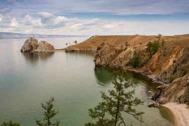 Şamanka Kayası ve Sibirya 'nın doğusundaki Baykal Gölü' nün Olkhon Adası 'nın ana köyü Khuzhir yakınlarında bulutlu bir günde kıyıların dağlık kesimi. Fotoğraf Temmuz 'da yazın çekildi..
