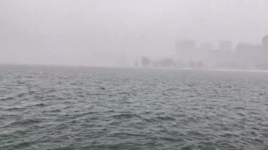 Arka planda şehir olan bir gölün üzerinde şiddetli kar yağışı