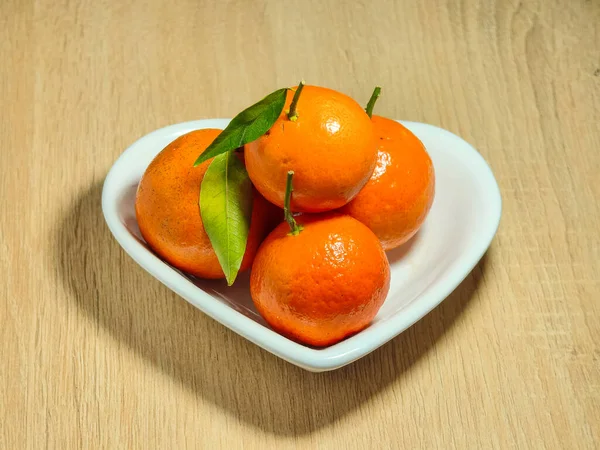 Beyaz kalp şeklinde bir tabakta olgun turuncu mandalinalar.