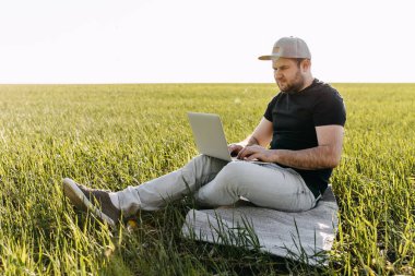 Şapkalı adam sahada dizüstü bilgisayarla çalışıyor.
