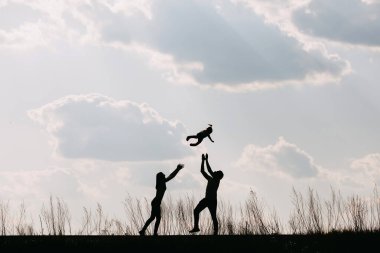 Siluetler mutlu, genç bir aile doğada birlikte vakit geçiriyor.