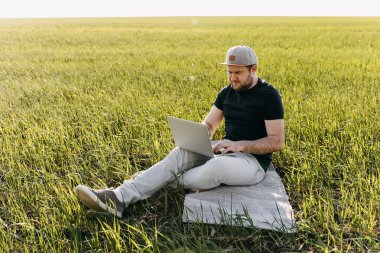 Şapkalı adam sahada dizüstü bilgisayarla çalışıyor.