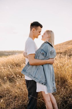 Gün batımında çayırda kucaklaşan güzel genç çift.