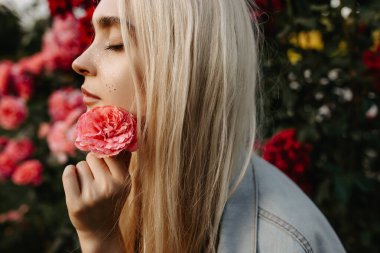 Bahçedeki güllerin önünde çiçek tutan güzel bir kadının portresi.