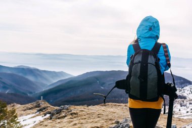 Sırt çantalı bir kadının dağlarda yürüyüşünün arka görüntüsü.