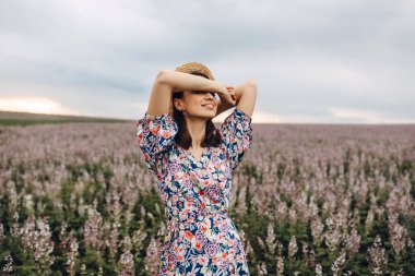 Çiçekli çayırlarda saman şapkalı ve elbiseli güzel bir kadının portresi.