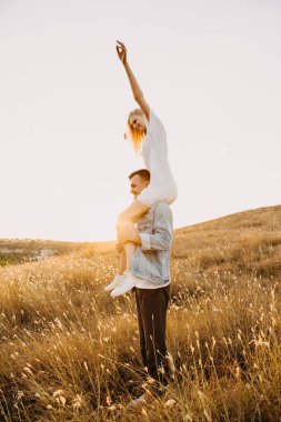 Güzel genç bir kadın gün batımında erkek arkadaşının omuzlarında çayırda