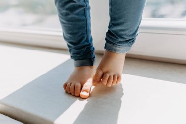 Pencere kenarında duran küçük bir çocuğun kırpılmış ayak görüntüsü.