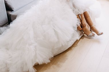 Beyaz elbiseli, yüksek topuklu bir gelin kanepeye oturuyor.