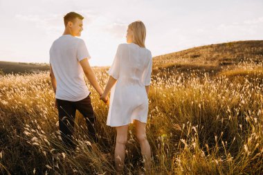 Gün batımında çayırda el ele tutuşan güzel genç bir çift.