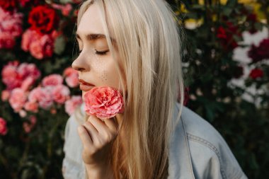 Bahçedeki güllerin önünde çiçek tutan güzel bir kadının portresi.