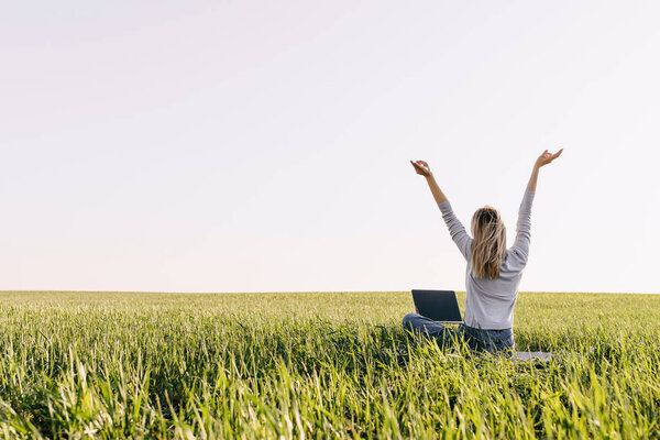 beautiful young woman working with laptop on green field