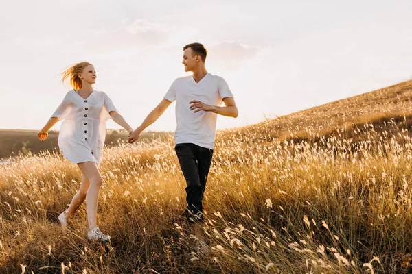 美しい若いカップルは日没時に牧草地で楽しんでいます — ストック写真
