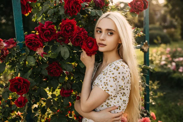庭のバラの茂みの前で美しい若い女性の肖像画 — ストック写真