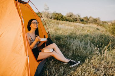 güzel genç bayan kamp çadırında oturuyor ve doğada akşam yemeği yiyor.