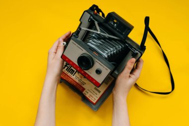 Kadının sarı arka planda klasik polaroid fotoğraf makinesini tutarken yakın plan fotoğrafı.