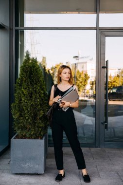 Şehir sokaklarında dizüstü bilgisayarı ve iş evrakları olan güzel genç bir kadın.