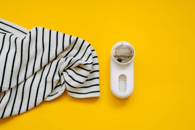 Giysilerdeki topakları sarı arkaplanda elektrikli budayıcı ile çıkartırken yakın çekim.