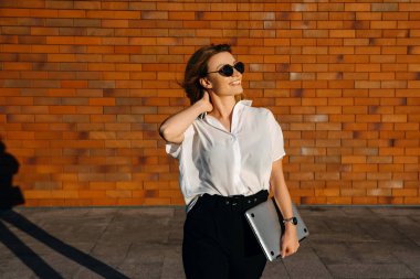 Kırmızı tuğla duvarın önünde dizüstü bilgisayarı olan güzel genç bir kadın.