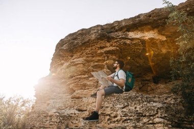 Elinde kağıt haritayla dağda oturan yakışıklı bir gencin portresi.