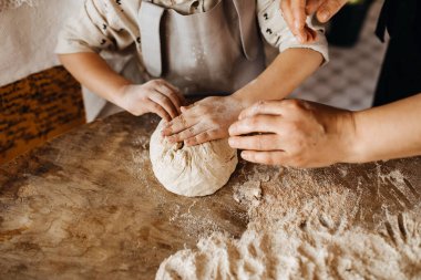 Çocuk ve anne elleriyle hamur yoğurur.