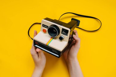 Kadının sarı arka planda klasik polaroid fotoğraf makinesini tutarken yakın plan fotoğrafı.