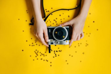 Sarı masa üstünde parıltıları olan instax kameralı bir kadının üst görüntüsü