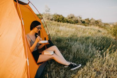 güzel genç bayan kamp çadırında oturuyor ve doğada akşam yemeği yiyor.