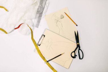Beyaz masadaki moda tasarımcısı çizimleri ve makasları
