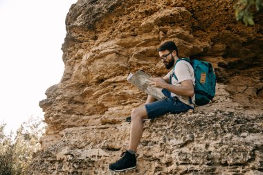 Elinde kağıt haritayla dağda oturan yakışıklı bir gencin portresi.