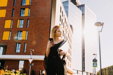 Şehir sokaklarında dizüstü bilgisayarı ve iş evrakları olan güzel genç bir kadın.