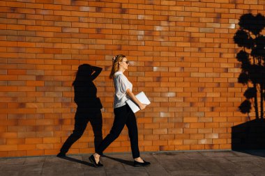 Kırmızı tuğla duvarın önünde dizüstü bilgisayarı olan güzel genç bir kadın.