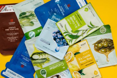 Sarı arka planda yüz maskesi paketleri taşıyan bir kadının kırpılmış fotoğrafı.