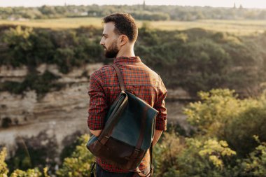 Doğada deri çantalı yakışıklı genç bir adamın portresi.