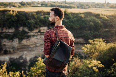 Doğada deri çantalı yakışıklı genç bir adamın portresi.