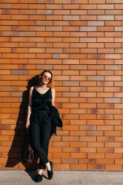 Caddedeki güzel genç kadın kırmızı tuğla duvarın önünde
