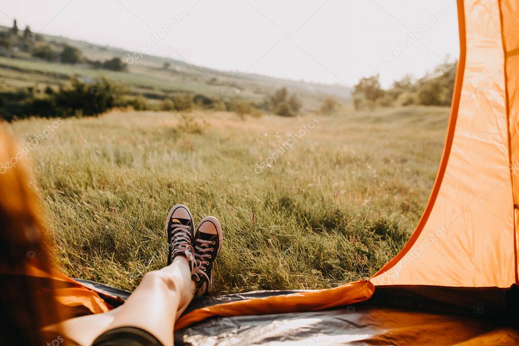 close-up shot of legs of young woman sitting in camping tent on sunny evening