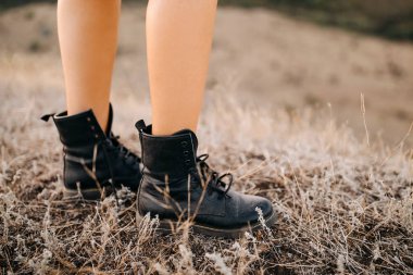 Çayırda siyah deri çizmeli bir kadın.