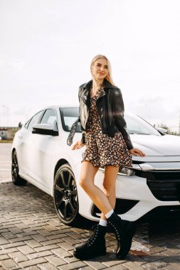 Güzel genç bir kadın arabasının önünde duruyor.