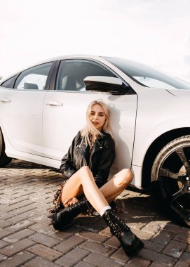 Güzel genç bir kadın park yerinde arabasının önünde oturuyor.