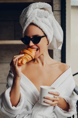 Ayçöreği ve bir fincan kahveyle havluyla ve bornozuyla otelde dinlenen güzel genç bir kadın.