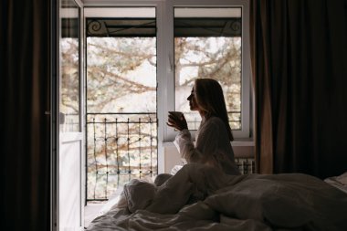 Güzel genç bayan, sabahları yatakta kahve içiyor.