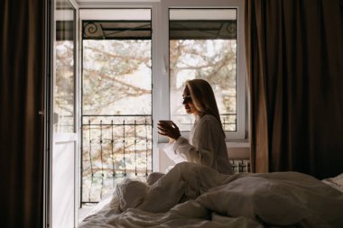 Güzel genç bayan, sabahları yatakta kahve içiyor.