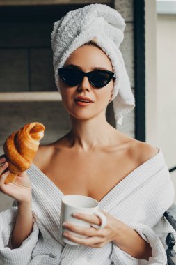 Ayçöreği ve bir fincan kahveyle havluyla ve bornozuyla otelde dinlenen güzel genç bir kadın.