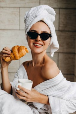 Ayçöreği ve bir fincan kahveyle havluyla ve bornozuyla otelde dinlenen güzel genç bir kadın.